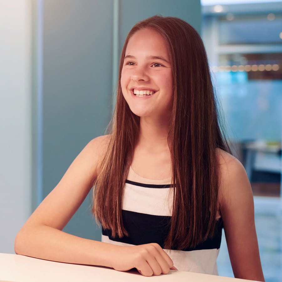 A young girl with long brown hair smiles at the reception desk.